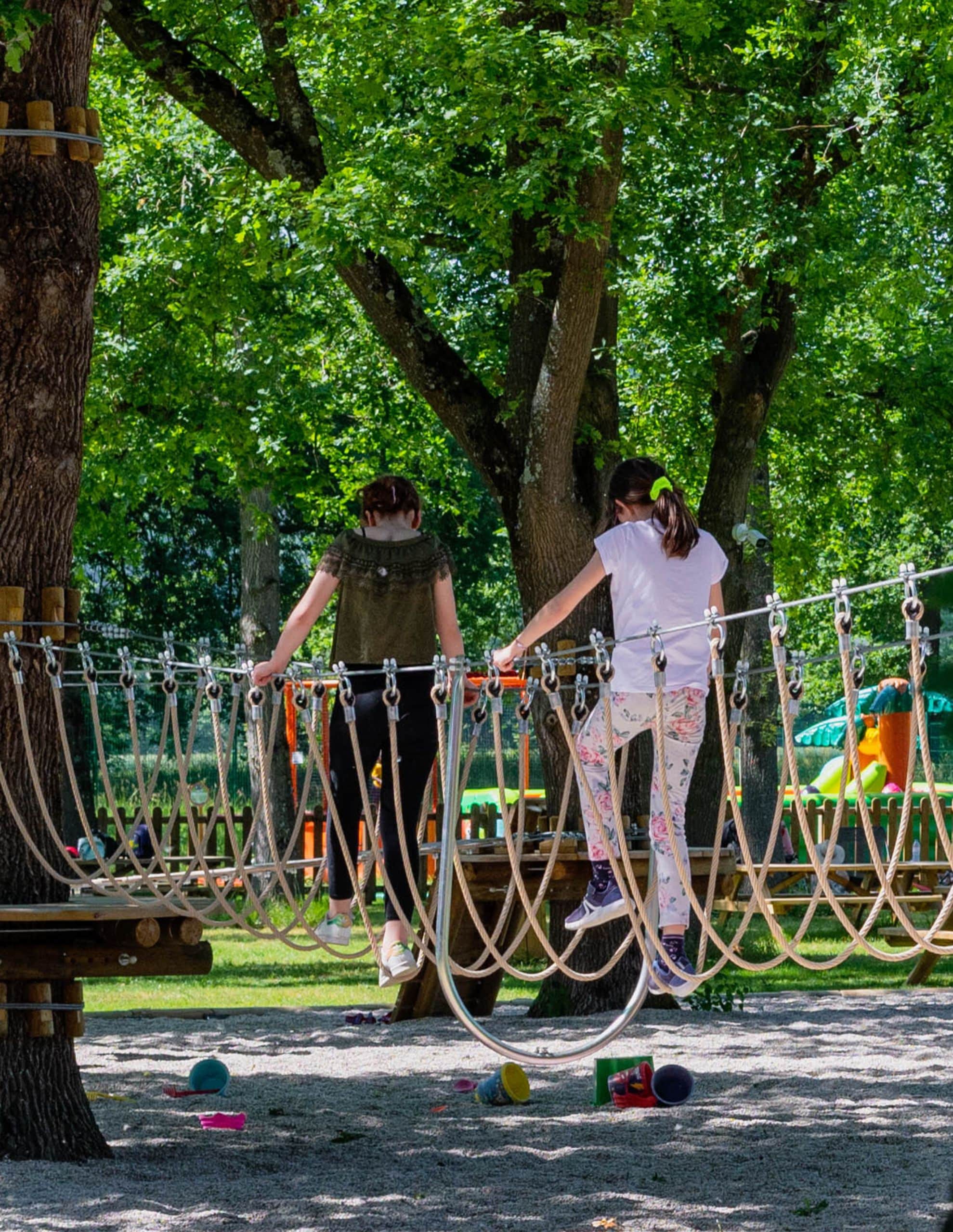 Enfants qui font le parcours d'accrobranche de Loupy Park sous les arbres en feuilles. Les enfants sont sur l'atelier des cordes en U.
